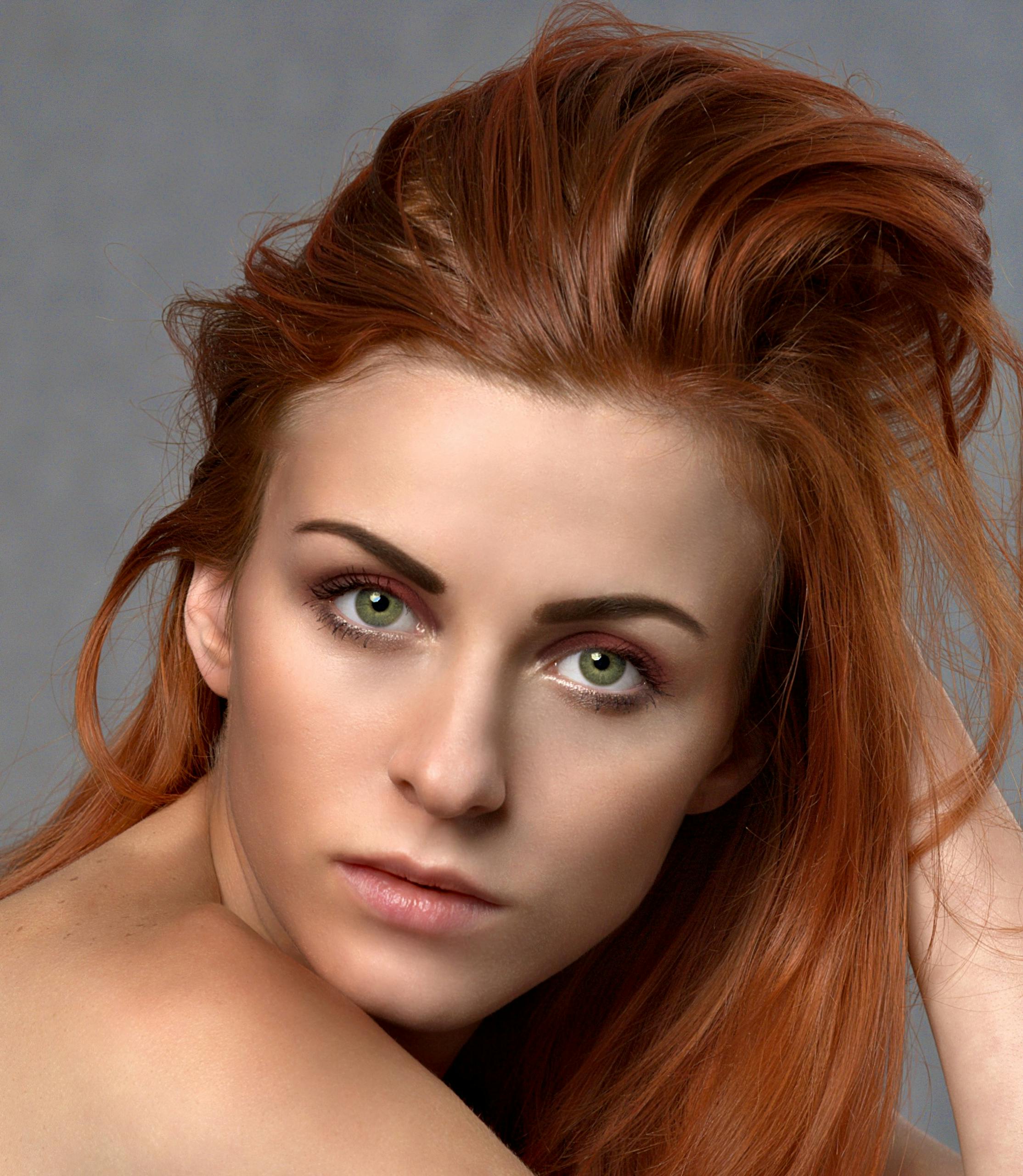 Close-up portrait of a woman with striking red hair and green eyes, exuding elegance.